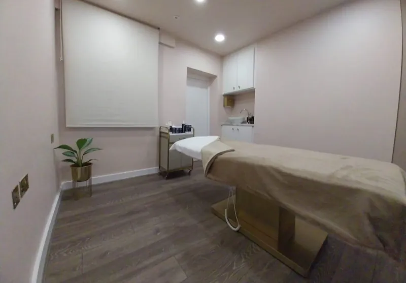 A bright massage room with a heated couch, product trolley and washbasin